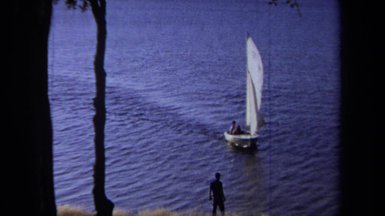 White sailboat farther across the lake with a person silhouetted near the shoreline.