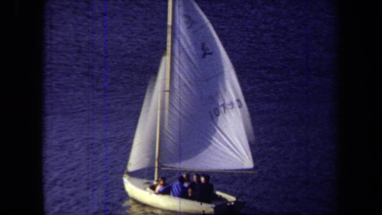 1971 California 8mm frame showing a small white sailboat with several passengers on calm blue water.