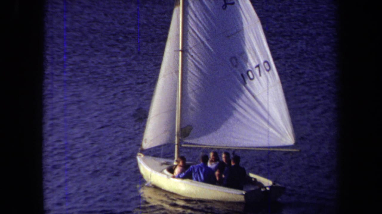 Sailboat with several people seated beneath a numbered sail.