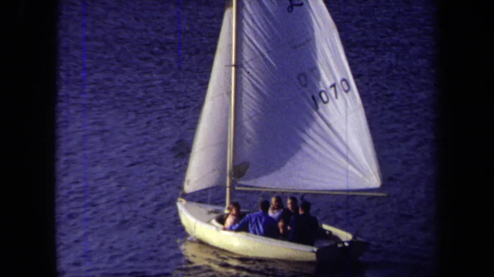 The sailboat marked 1070 carries several visible passengers across calm water in this 1971 California home-movie frame.