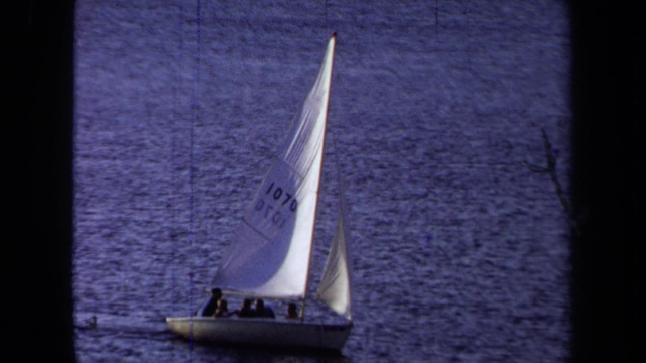 1971 California 8mm frame showing a white sailboat with passengers and a numbered sail moving across calm coastal water.