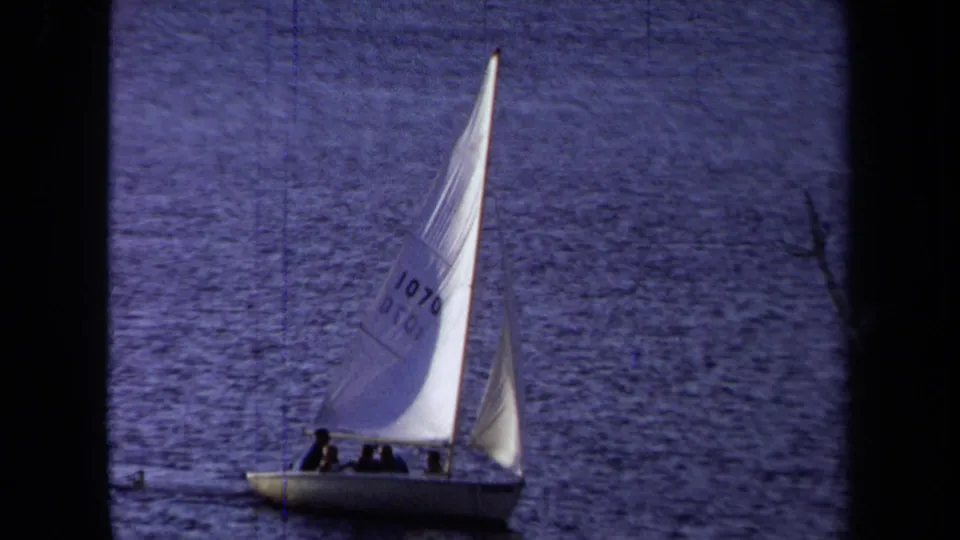 1971 California 8mm frame showing a white sailboat with passengers and a numbered sail moving across calm coastal water.