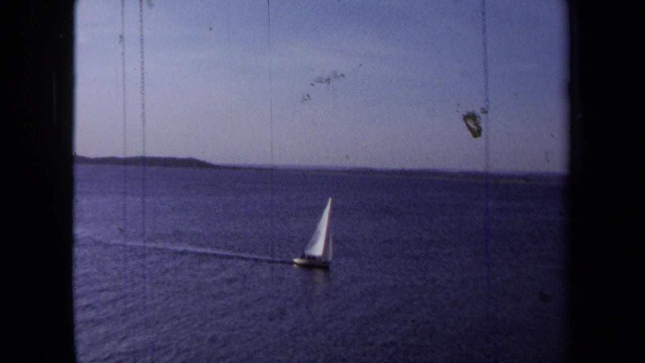 1971 California home-movie frame showing a small white sailboat crossing open water beneath a clear sky.