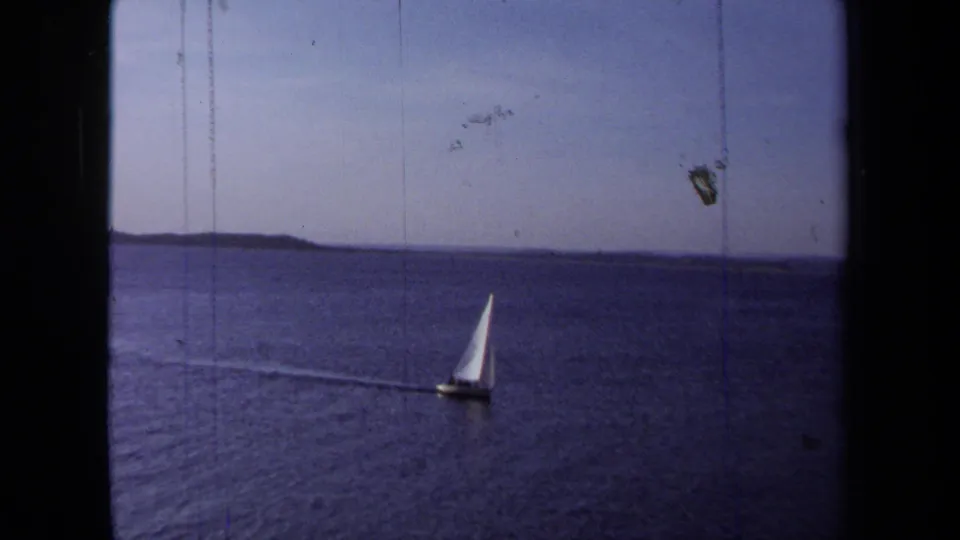 1971 California home-movie frame showing a small white sailboat crossing open water beneath a clear sky.