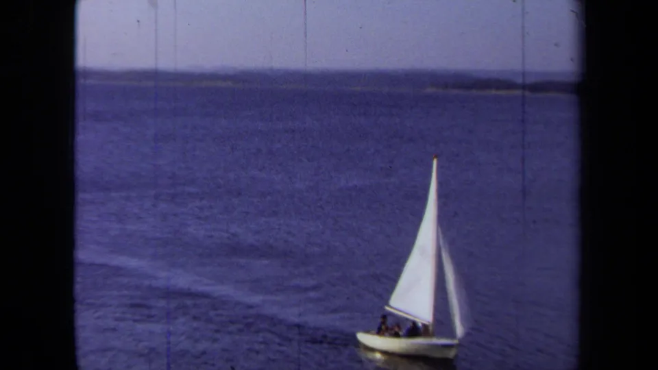 1971 California home-movie frame with a white sailboat carrying several people on open water.