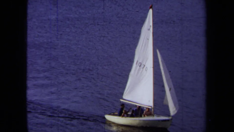 1971 California home-movie frame of sailboat 1070 carrying people across calm coastal water.