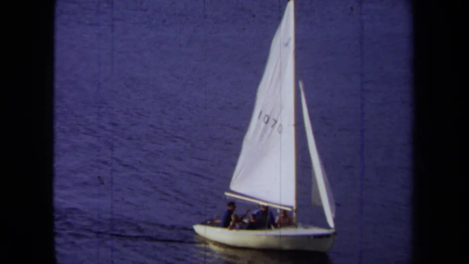 1971 California sailing frame with a white boat, numbered sail, passengers, and dark blue water in the background.