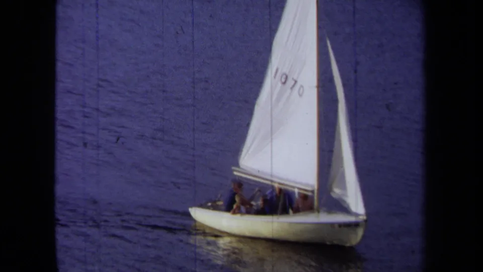 1971 California 8mm frame showing the small sailboat nearer in view, with passengers beneath a white sail marked 1070.