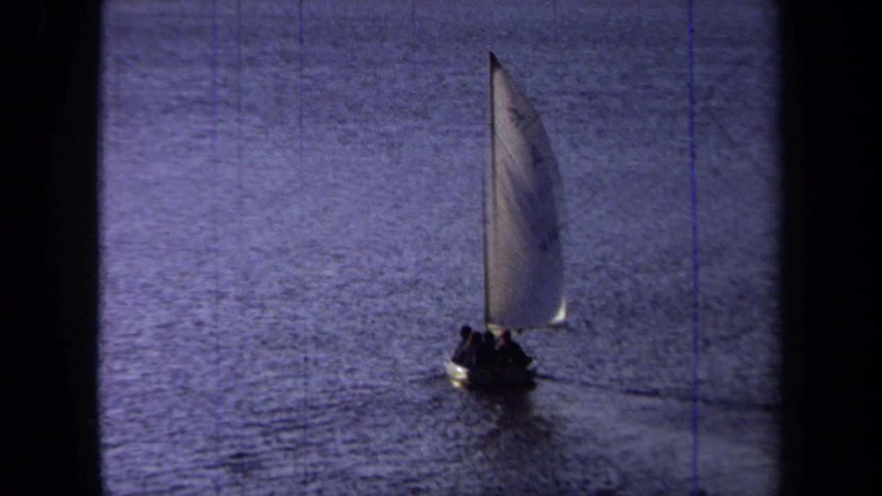 1971 California 8mm frame showing a small sailboat carrying silhouetted passengers across calm blue water.