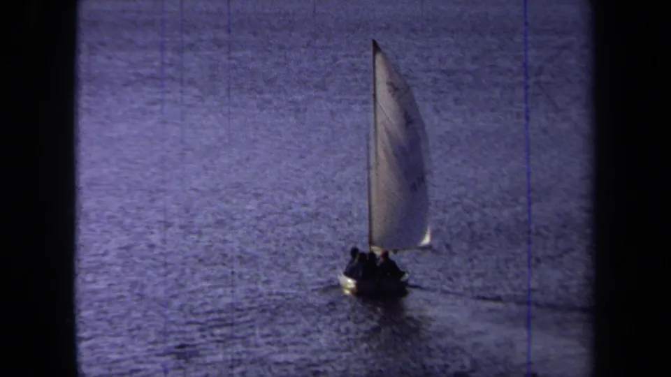 1971 California 8mm frame showing a small sailboat carrying silhouetted passengers across calm blue water.