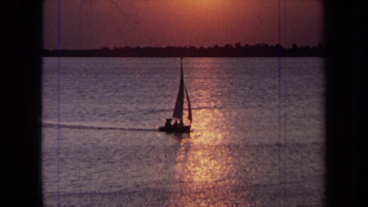 1971 California 8mm frame of a small sailboat silhouetted on calm water beneath a warm sunset reflection.