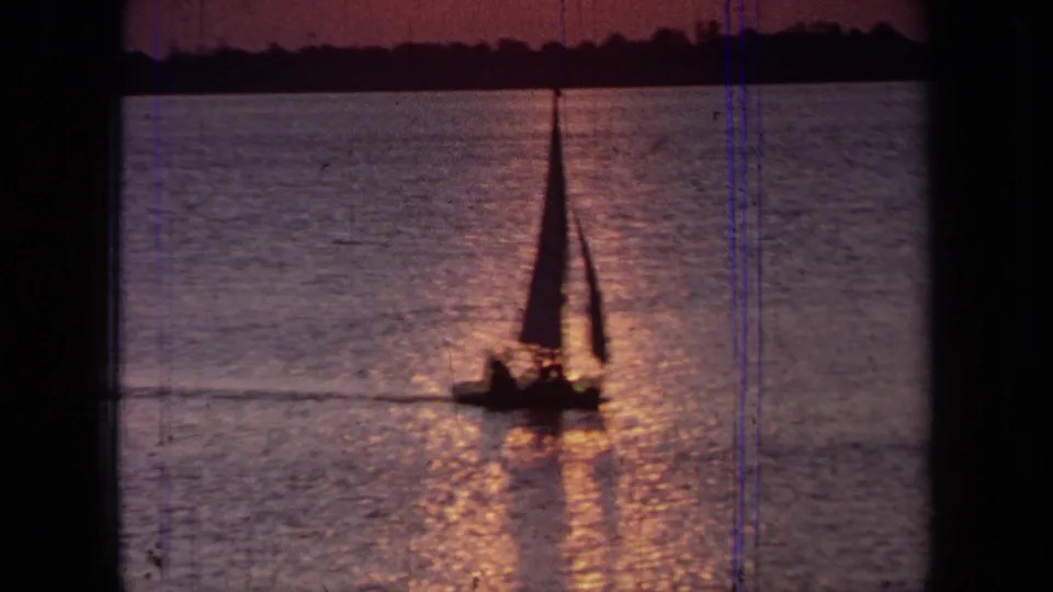 Small sailboat with passengers silhouetted on California water at sunset in a grainy 1971 8mm home-movie frame.
