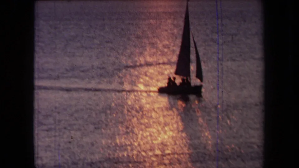 Closer 1971 California home-movie view of a small sailboat and silhouetted passengers moving through sunset glare.