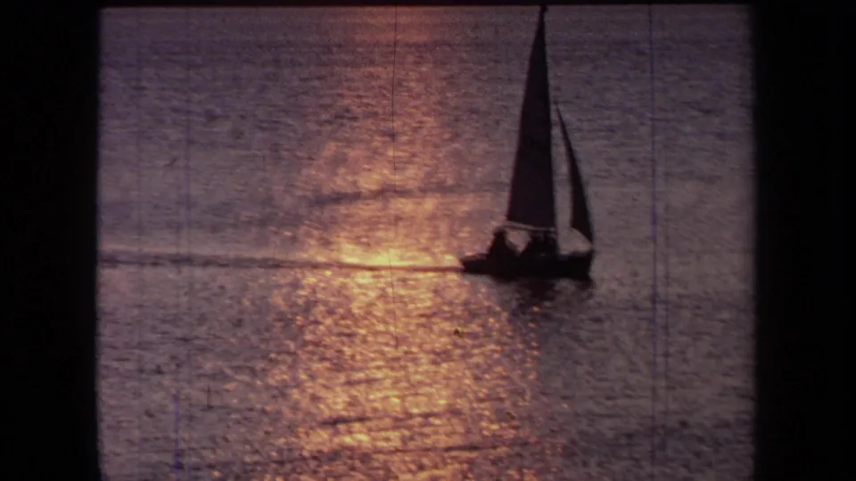 1971 California 8mm frame of a sailboat silhouetted beside a bright sunset path across the water.