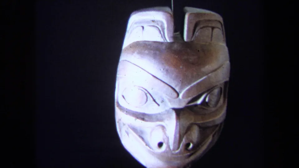 Close 1971 8mm frame of a carved mask rotating or displayed against a dark background; cultural origin is not identified.