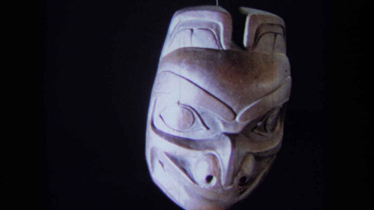 1971 8mm frame showing a carved wooden mask from the front, lit against a dark backdrop in California metadata context.