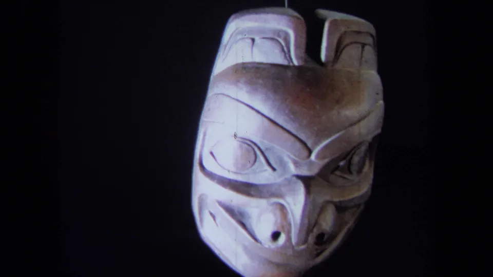 1971 8mm frame showing a carved wooden mask from the front, lit against a dark backdrop in California metadata context.