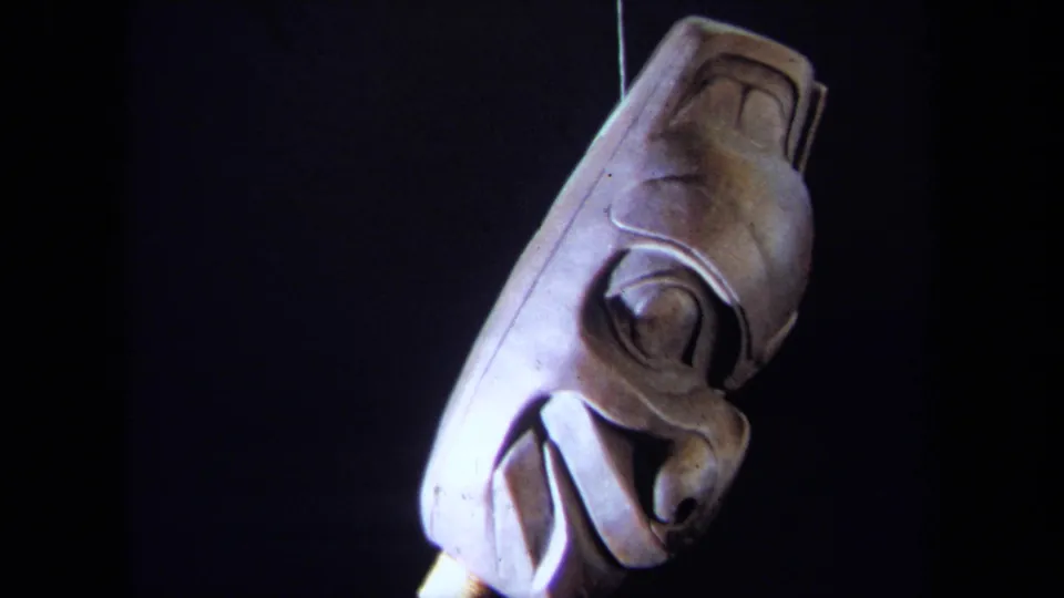 1971 8mm frame showing the suspended carved mask turned to the side under focused light.