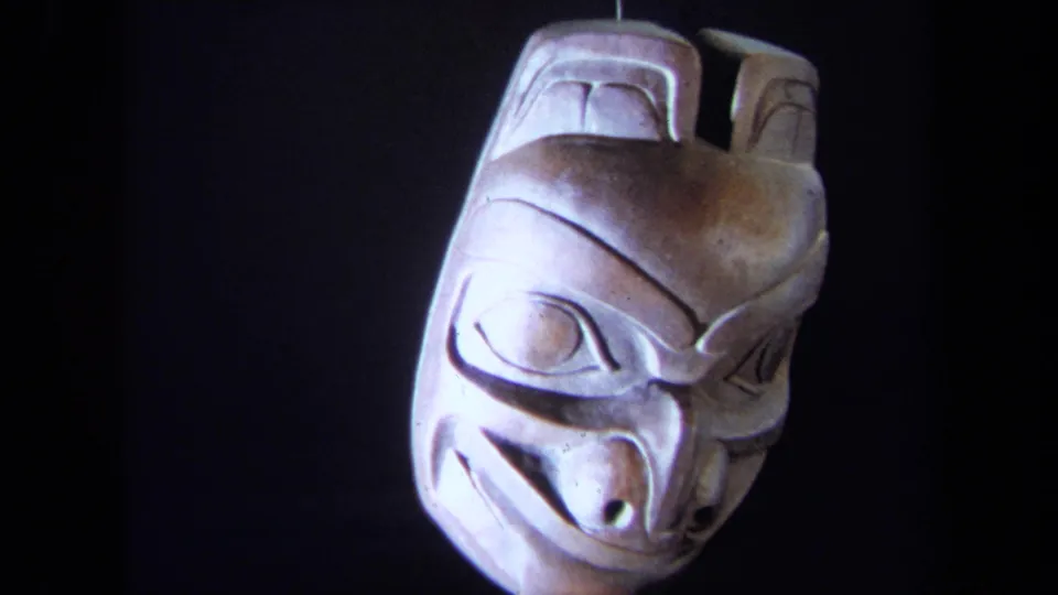 1971 8mm frame showing the mask at a slight angle, with carved facial lines and uneven spotlighting visible.