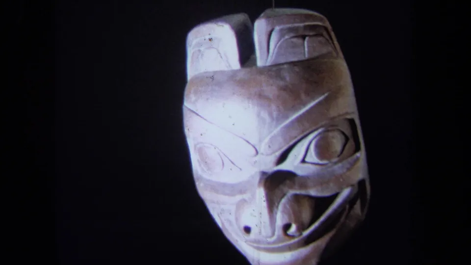 1971 8mm frame showing the carved mask nearly front-on, with one side brightly lit and the other in shadow.