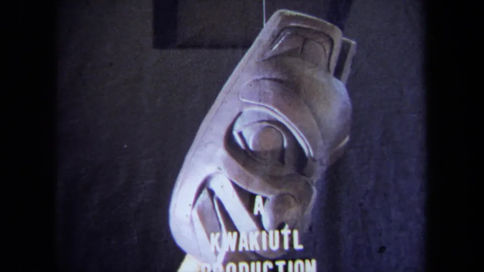 1971 California 8mm frame showing the pale carved mask from a side angle with visible “A KWAKIUTL PRODUCTION” text.
