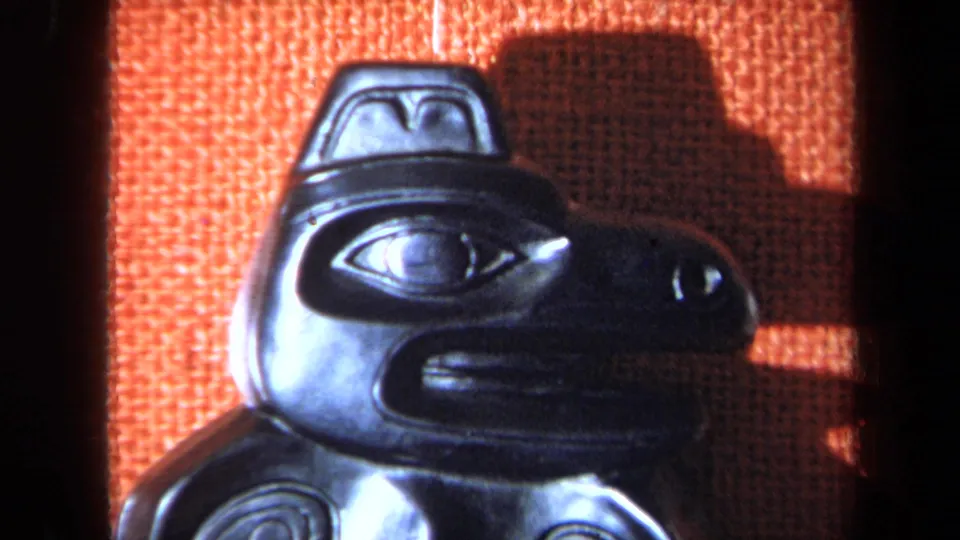 1971 California 8mm frame showing a dark glossy carved mask in profile against an orange textured background.