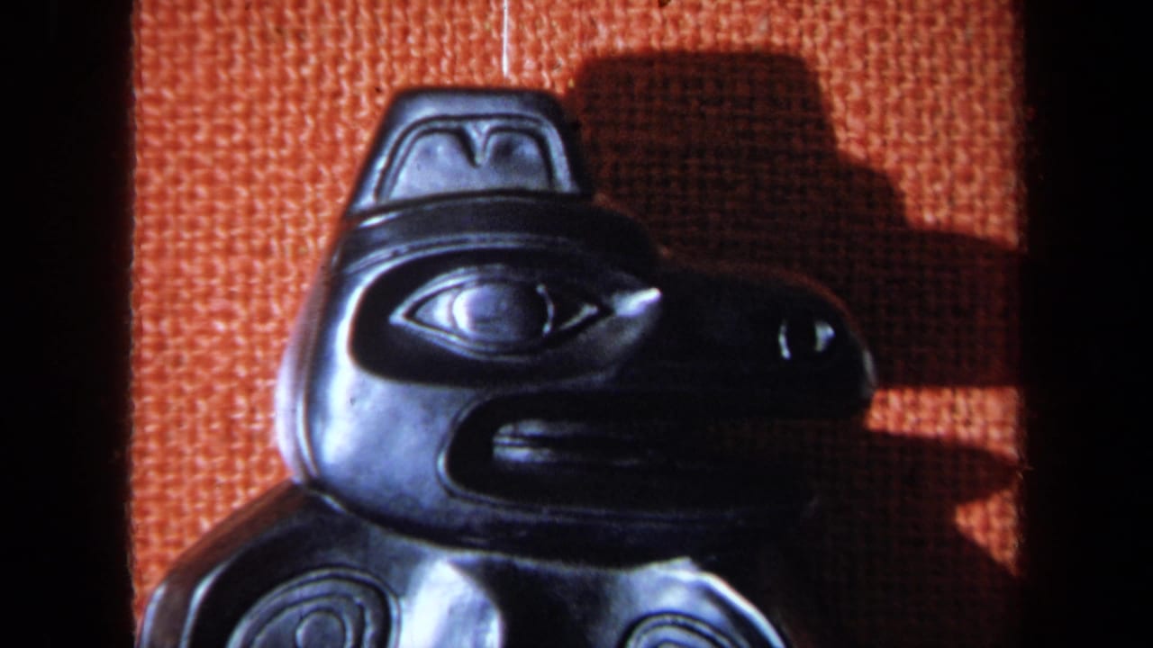 1971 8mm frame showing a close view of a black carved bird figure, likely part of a cultural display, against orange woven fabric.