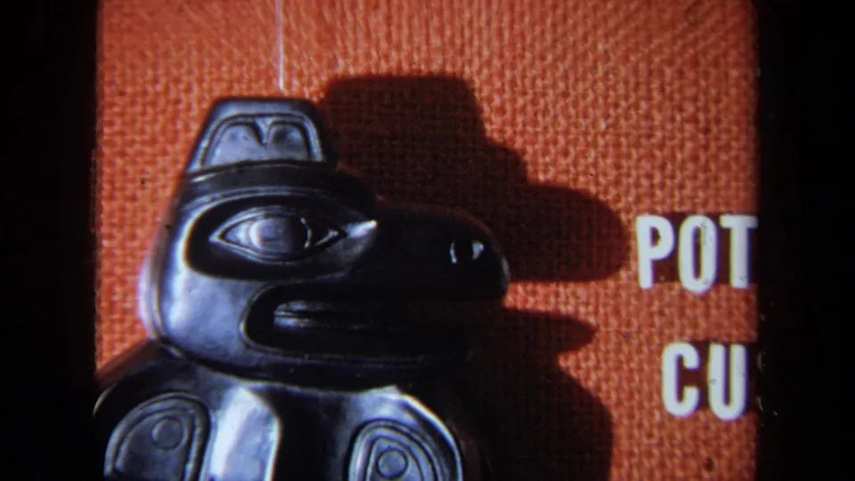 1971 8mm frame with the black carved bird figure at left and partial white Potlatch Customs display text entering at right.