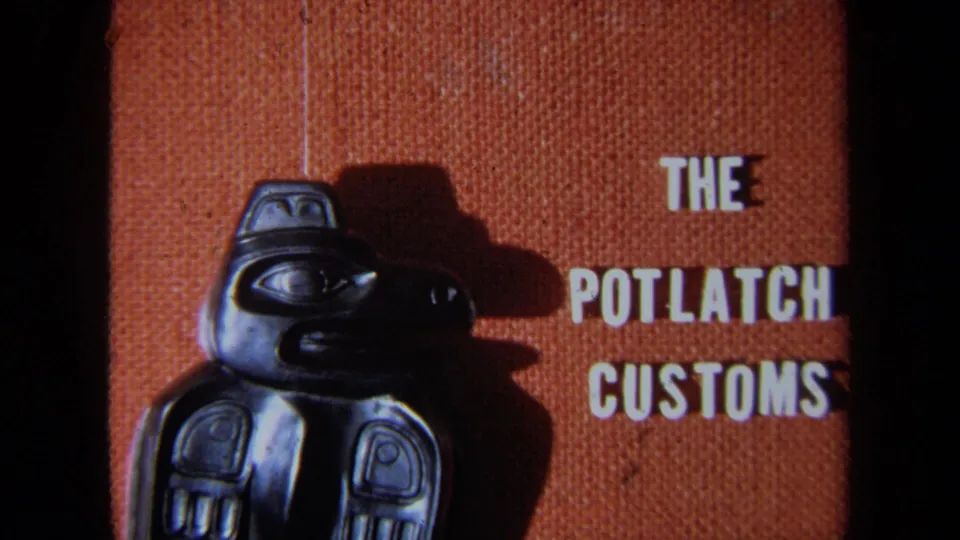 1971 8mm frame in California showing the carved bird figure beside clear white display text reading The Potlatch Customs.