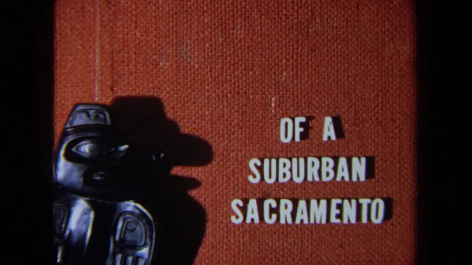 1971 California 8mm frame with a cropped dark carved figure and white block words Of a Suburban Sacramento.