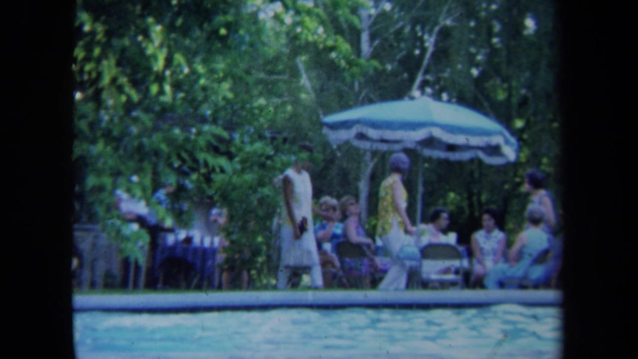 1971 California 8mm frame showing adults gathered beside a backyard swimming pool under a patio umbrella.