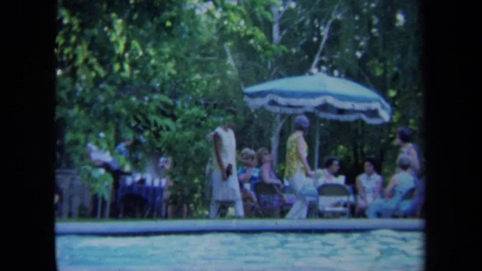 1971 California 8mm frame showing adults gathered beside a backyard swimming pool under a patio umbrella.