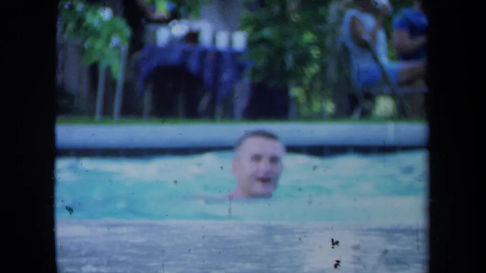 1971 California 8mm frame showing a smiling man in the pool with a relaxed backyard gathering behind him.