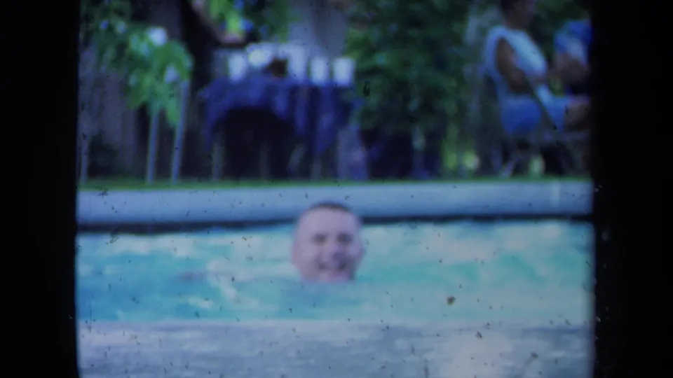 Adult man smiles from the water in a California pool scene, with trees and soft 8mm color in the background.
