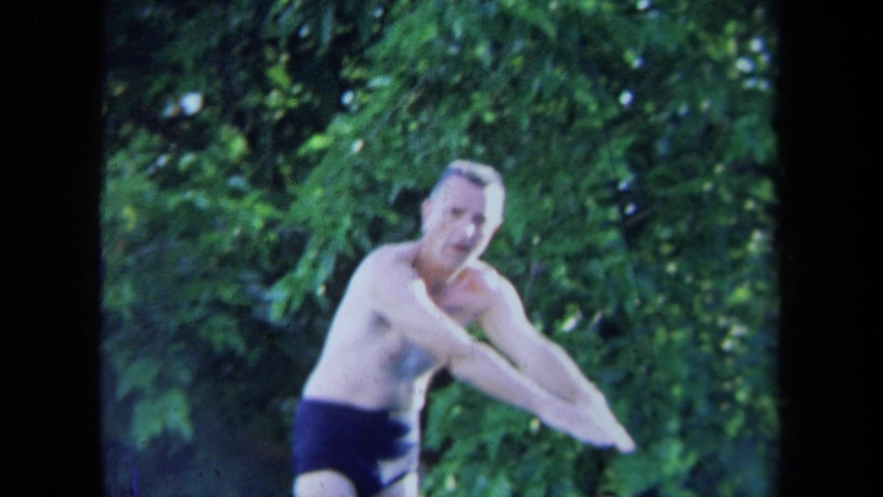 The diver leans forward in dark swim briefs, his face visible against leafy California poolside greenery.