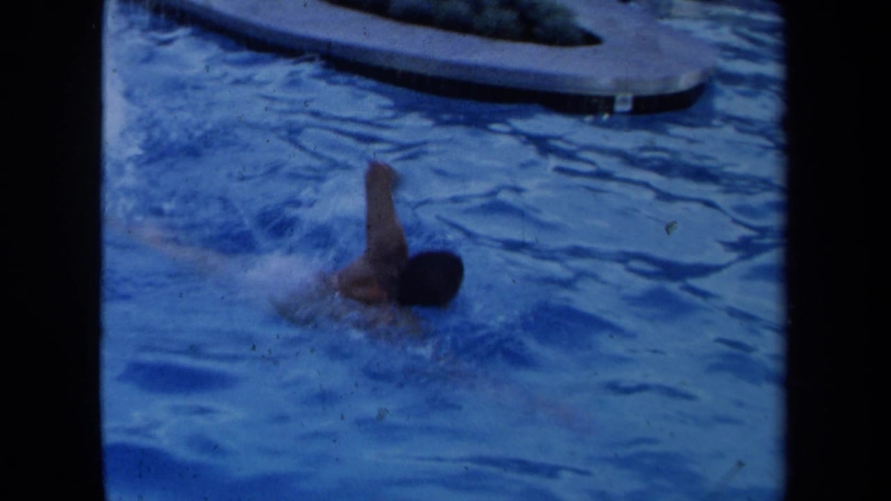 Adult swimmer doing a freestyle stroke in a blue pool with dark film borders.