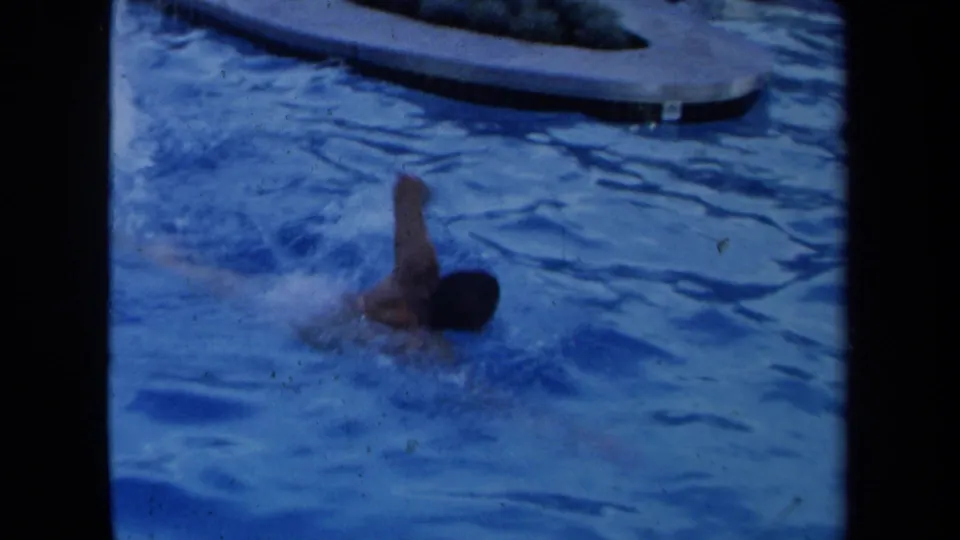 1971 California 8mm frame showing an adult swimmer mid-stroke in a backyard pool, with splashing water and contact-sheet borders.