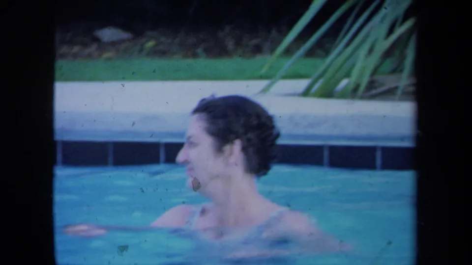 The swimmer appears in profile in the pool, laughing or speaking as the handheld Super 8 frame holds on her movement.