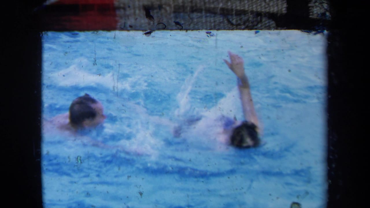 Two swimmers in a blue pool, one with an arm raised during a stroke.