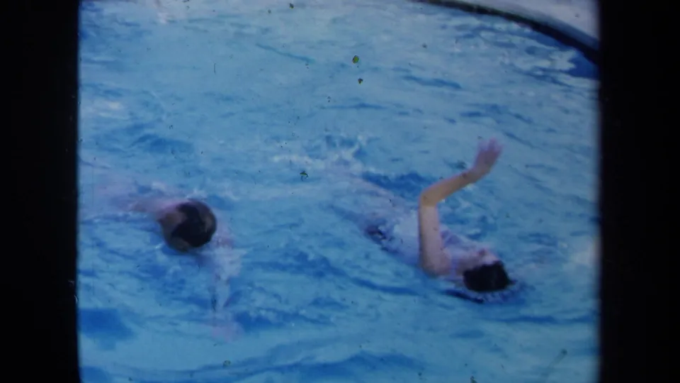 Final pool frame shows two swimmers apart in the water, one with an arm lifted during a stroke, in grainy 1971 8mm footage.