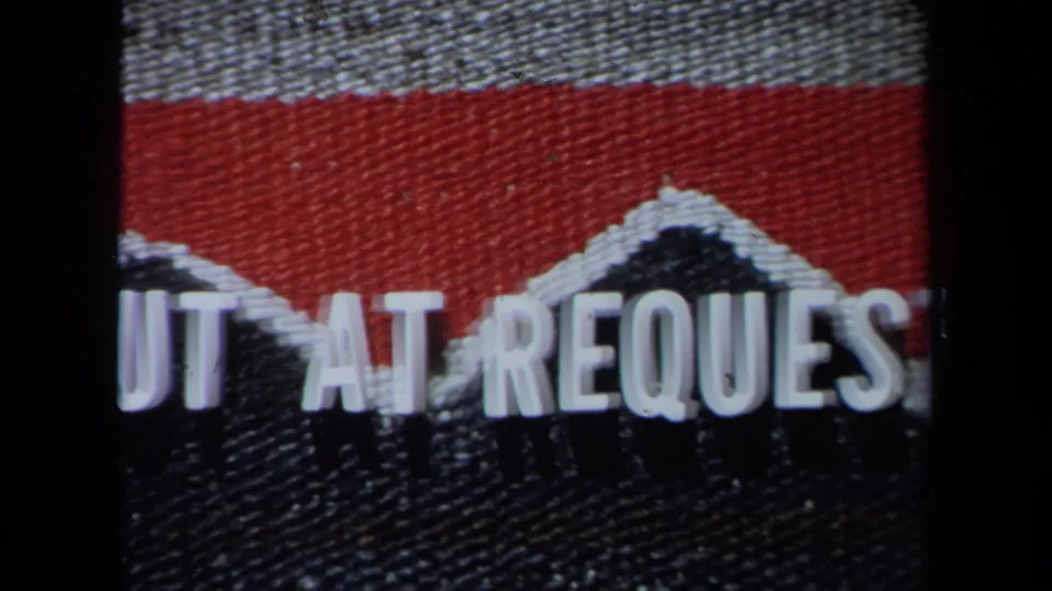 Cropped 8mm frame of a red and dark textured title card with partial white cut-at-request lettering.