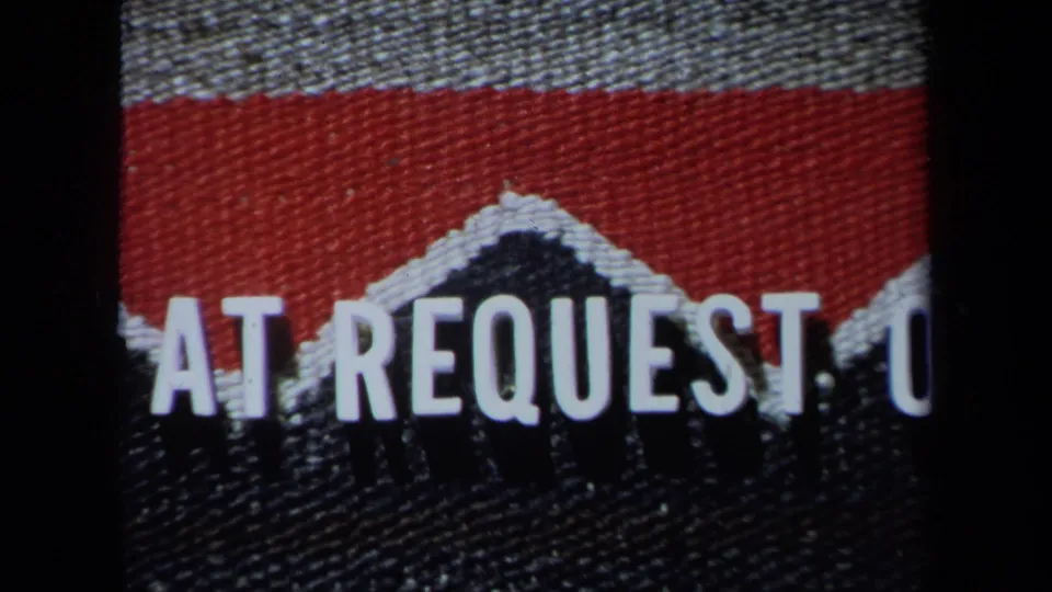 Home-movie editing card showing white AT REQUEST text on a red and dark woven-looking background.