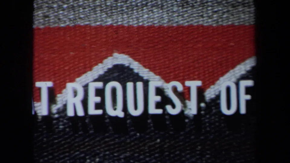 1971 California 8mm frame showing woven red and black fabric with cropped white block letters and dark film borders.