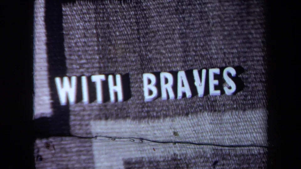 1971 California 8mm frame showing the phrase “WITH BRAVES” in white block letters on gray textured fabric.