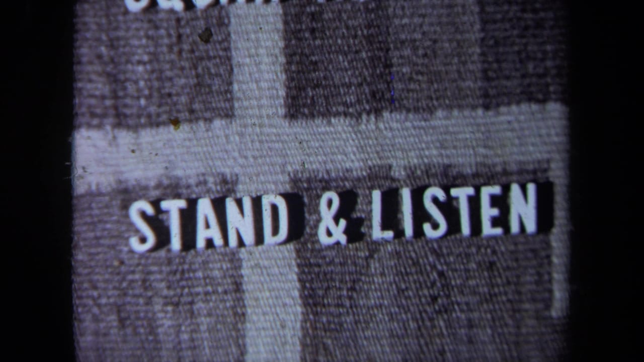 A filmed title-card or sign-like frame reads "STAND & LISTEN," with 8mm grain and dark frame borders visible.