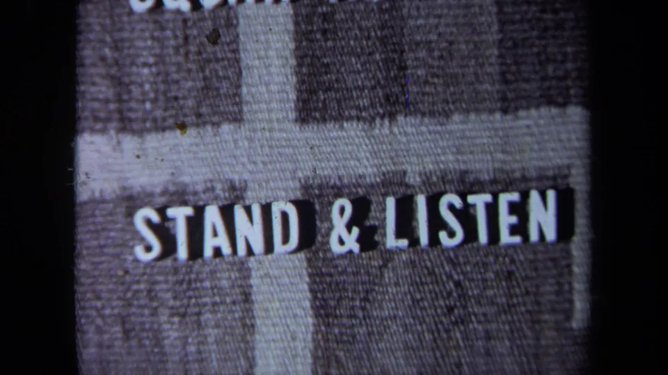 A filmed title-card or sign-like frame reads "STAND & LISTEN," with 8mm grain and dark frame borders visible.