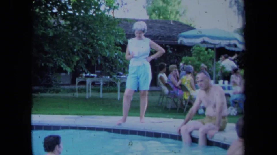 The backyard pool gathering continues, with a standing woman, seated man, and adults socializing under a green umbrella behind them.