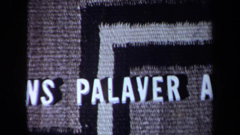 Close 8mm frame of the title card area, with partial white lettering over a woven patterned background.