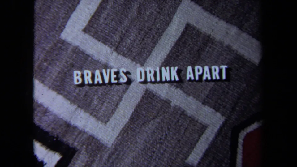 Close-up of textured fabric showing a swastika-like pattern and the words “BRAVES DRINK APART” in white lettering.