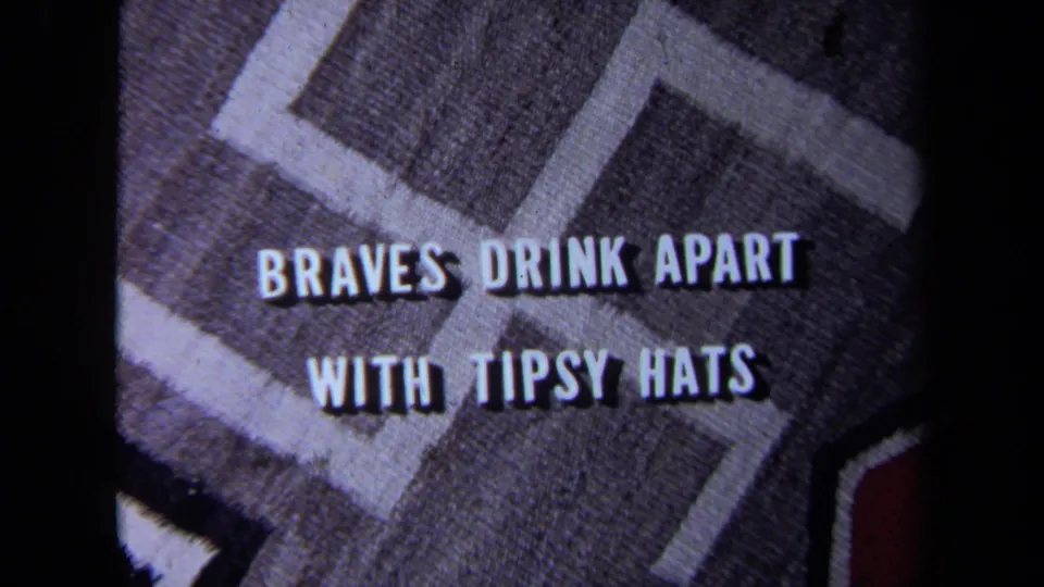 Close-up fabric frame with a swastika-like design and white slogan text reading “BRAVES DRINK APART WITH TIPSY HATS.”